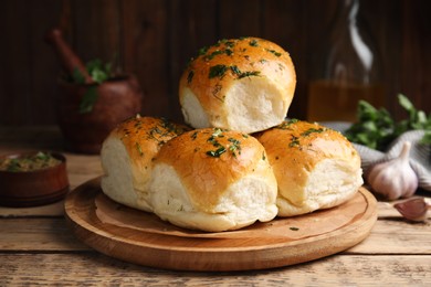 Traditional pampushka buns with garlic and herbs on wooden table Photo of Traditional pampushka buns with garlic and herbs on wooden table