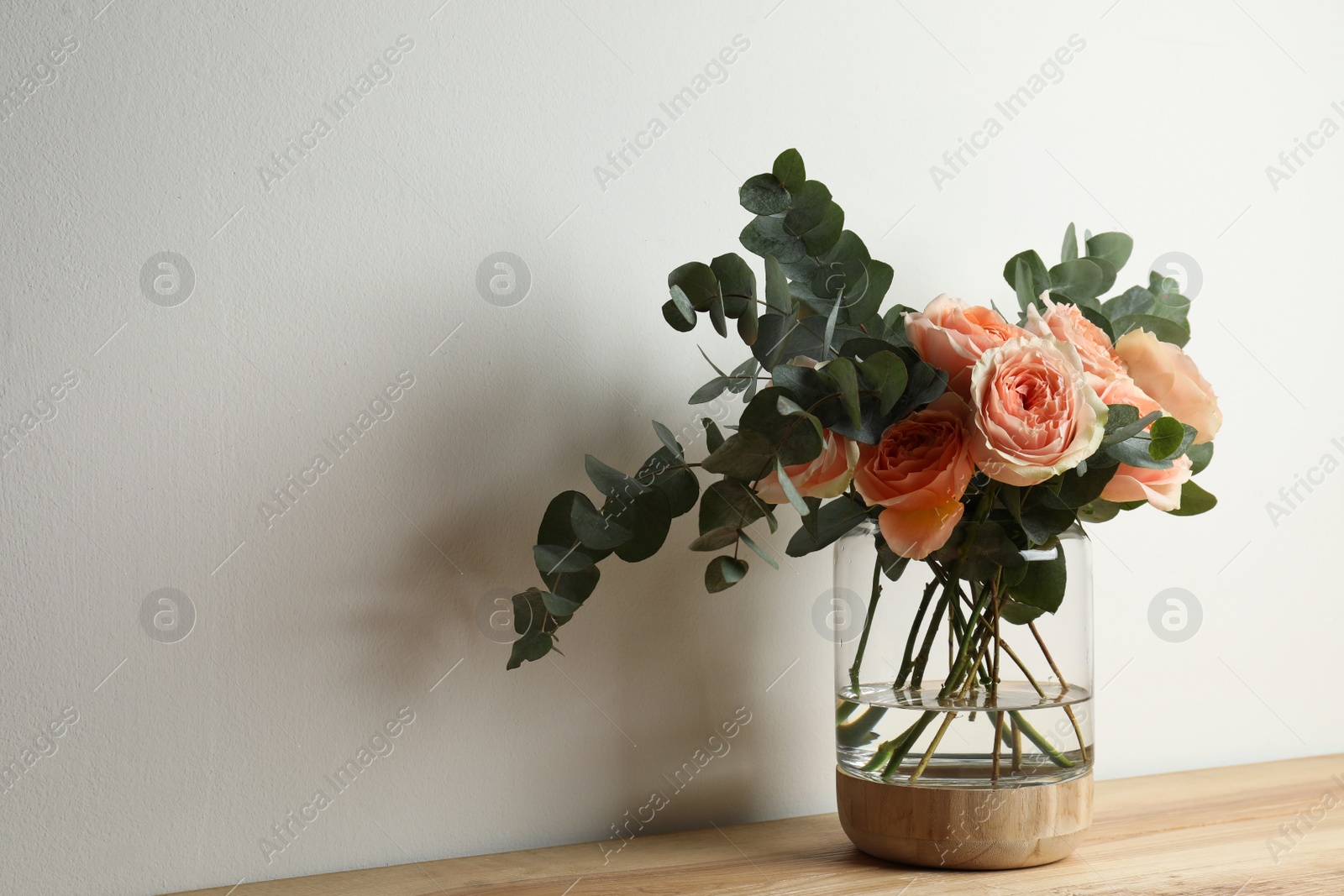Bouquet with beautiful flowers in glass vase on wooden table against white background. Space for text Photo of Bouquet with beautiful flowers in glass vase on wooden table against white background. Space for text