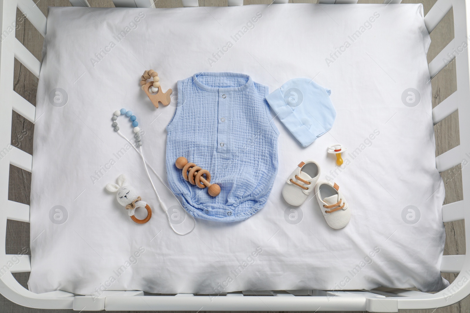 Flat lay composition with cute baby clothes and accessories on white bedsheet in crib Photo of Flat lay composition with cute baby clothes and accessories on white bedsheet in crib