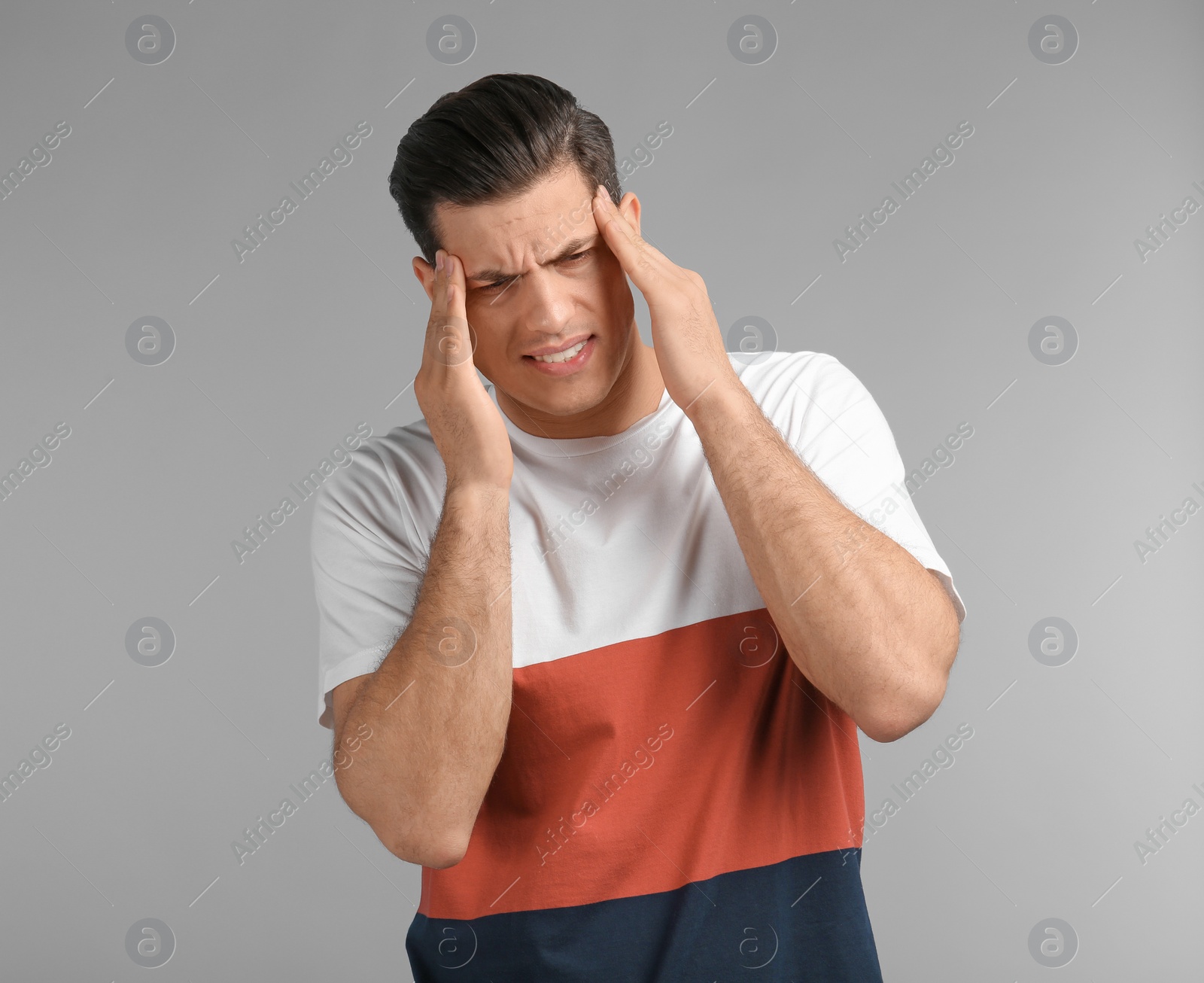 Young man suffering from headache on grey background Photo of Young man suffering from headache on grey background
