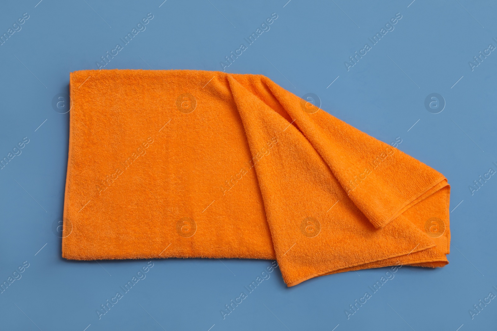 Photo of Folded orange beach towel on blue background, top view