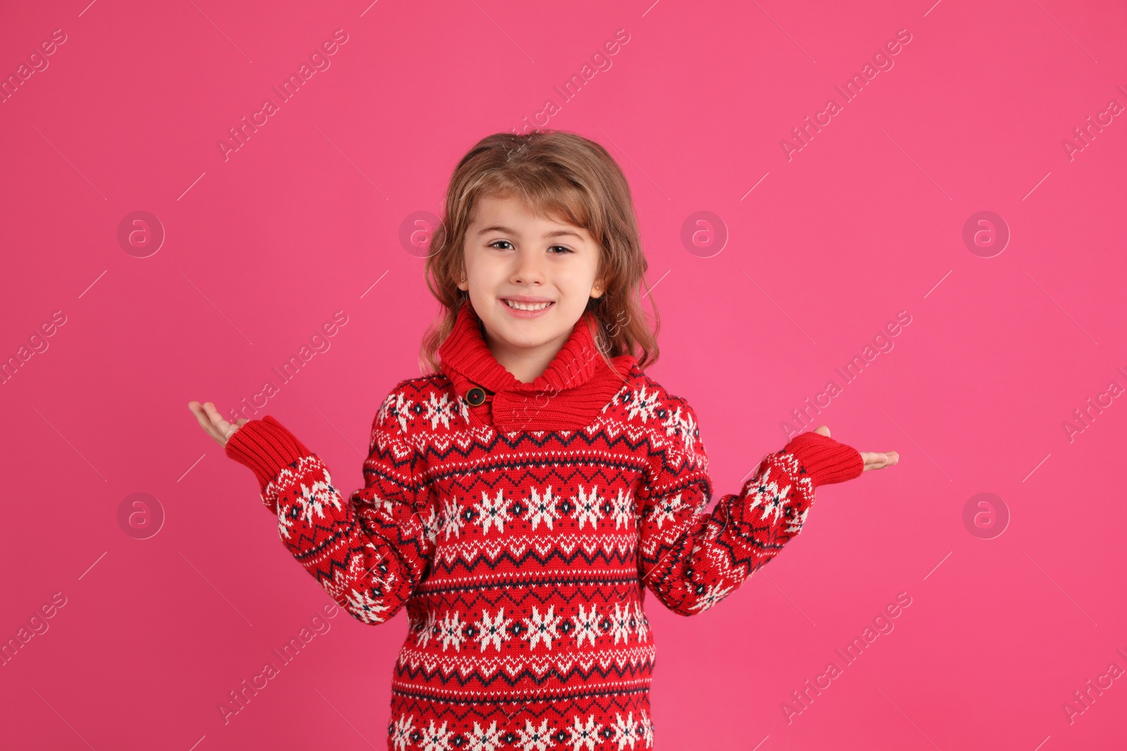 Photo of Cute little girl in red Christmas sweater smiling against pink background
