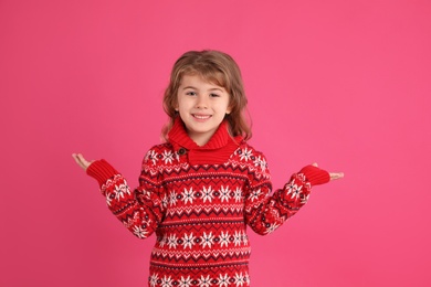 Photo of Cute little girl in red Christmas sweater smiling against pink background