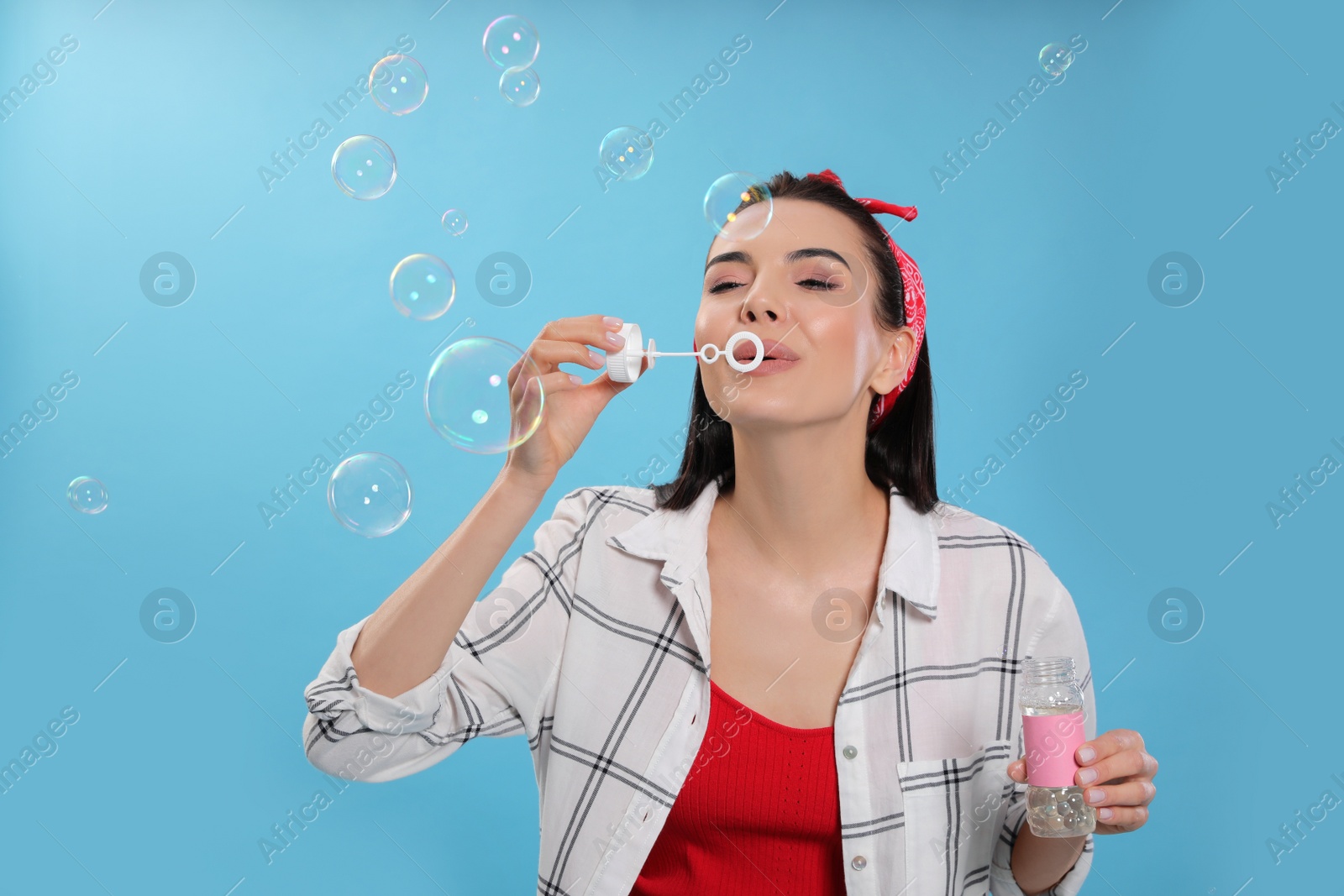 Young woman blowing soap bubbles on light blue background Photo of Young woman blowing soap bubbles on light blue background