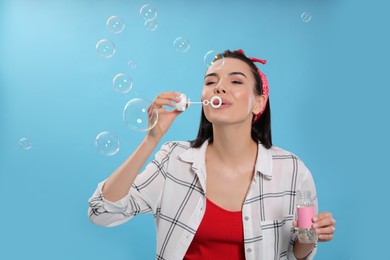 Young woman blowing soap bubbles on light blue background Photo of Young woman blowing soap bubbles on light blue background