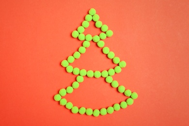 Christmas tree shape made with green fluffy balls on orange background, flat lay Photo of Christmas tree shape made with green fluffy balls on orange background, flat lay