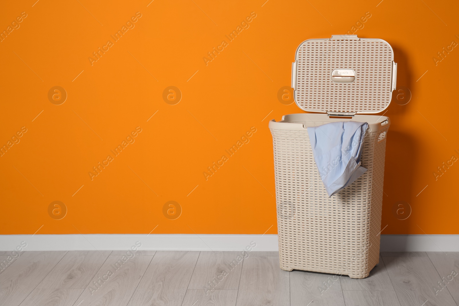 Open laundry basket with clothes near orange wall indoors, space for text Photo of Open laundry basket with clothes near orange wall indoors, space for text