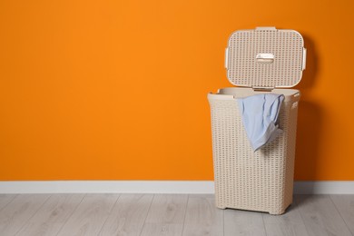 Open laundry basket with clothes near orange wall indoors, space for text Photo of Open laundry basket with clothes near orange wall indoors, space for text