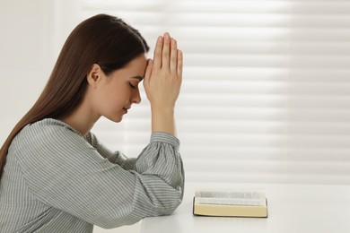 Religious young woman praying over Bible at table indoors Photo of Religious young woman praying over Bible at table indoors