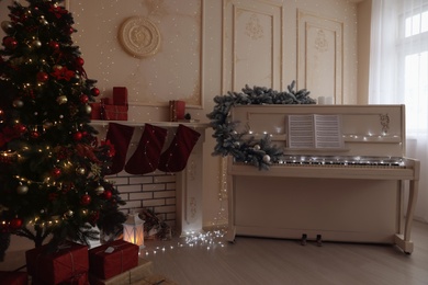 White piano with music sheets and beautiful Christmas tree in festive room interior Photo of White piano with music sheets and beautiful Christmas tree in festive room interior