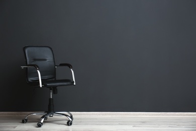 Comfortable office chair near black wall indoors. Space for text Photo of Comfortable office chair near black wall indoors. Space for text