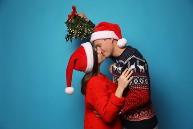 Happy couple kissing under mistletoe bunch on light blue background Photo of Happy couple kissing under mistletoe bunch on light blue background