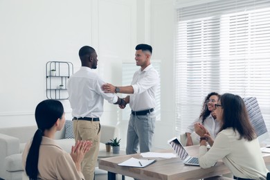 Boss shaking hand with new employee and coworkers applauding in office Photo of Boss shaking hand with new employee and coworkers applauding in office