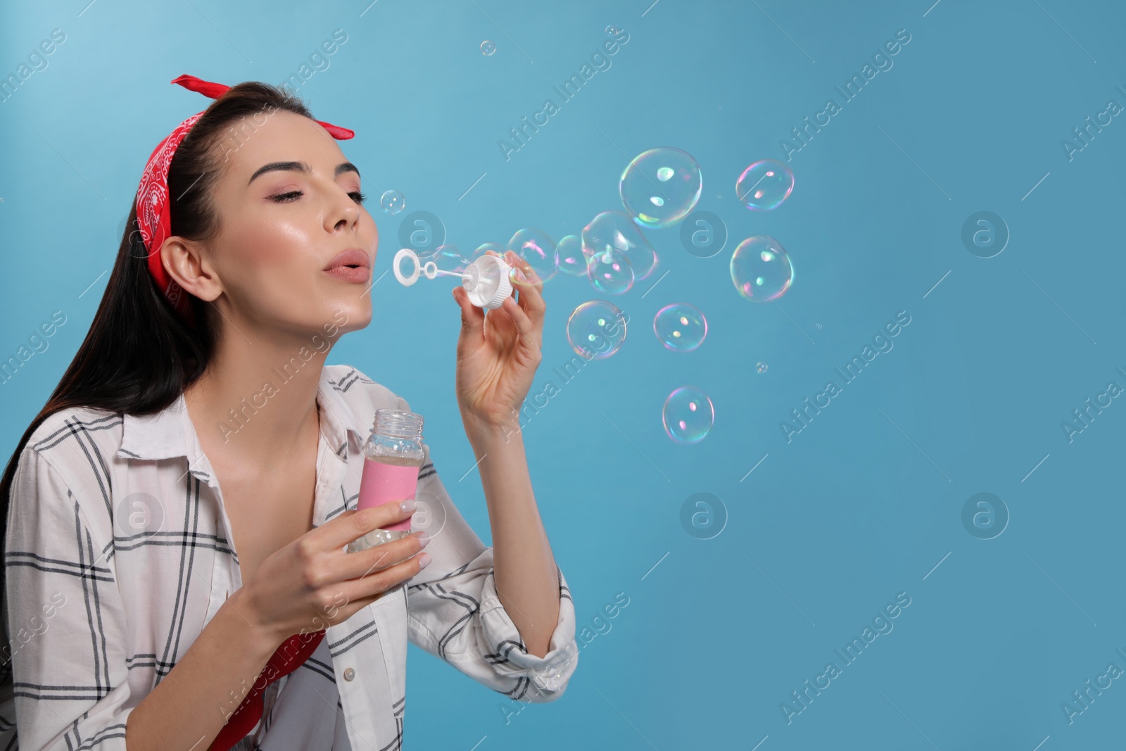 Young woman blowing soap bubbles on light blue background, space for text Photo of Young woman blowing soap bubbles on light blue background, space for text