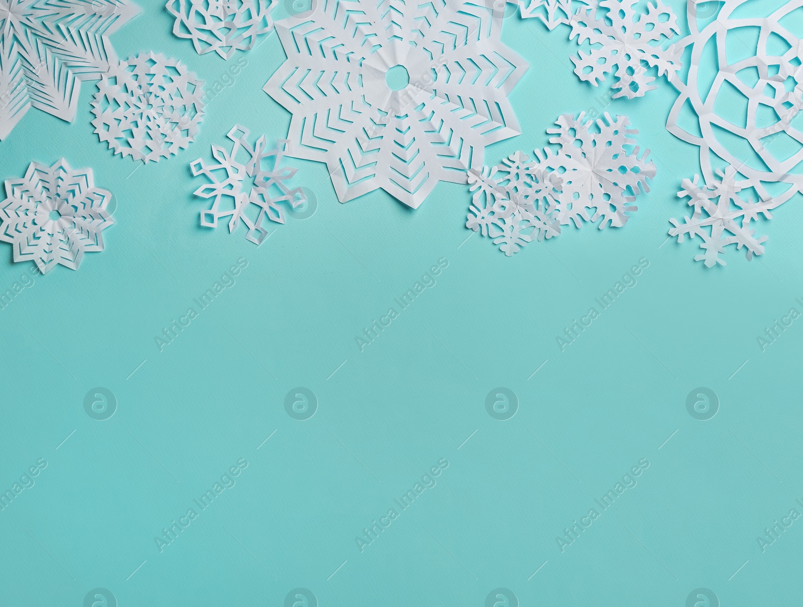 Flat lay composition with paper snowflakes on cyan background. Space for text Photo of Flat lay composition with paper snowflakes on cyan background. Space for text