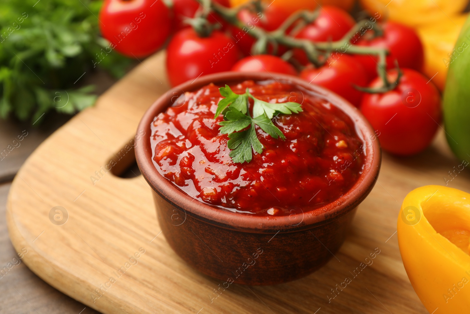 Delicious adjika sauce with parsley in bowl and ingredients on wooden board, closeup Photo of Delicious adjika sauce with parsley in bowl and ingredients on wooden board, closeup