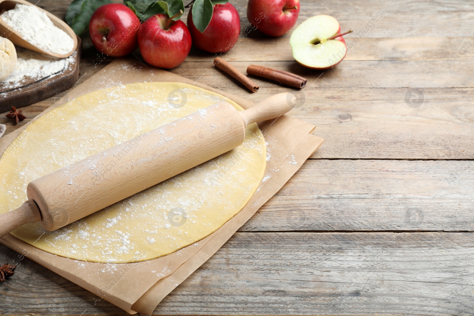 Rolling pin, raw dough and ingredients on wooden table, space for text. Baking apple pie Photo of Rolling pin, raw dough and ingredients on wooden table, space for text. Baking apple pie