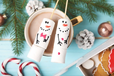 Flat lay composition with funny snowmen made of marshmallows in cup of hot drink on light blue wooden table Photo of Flat lay composition with funny snowmen made of marshmallows in cup of hot drink on light blue wooden table
