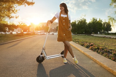 Young woman with kick scooter in sunny park Photo of Young woman with kick scooter in sunny park