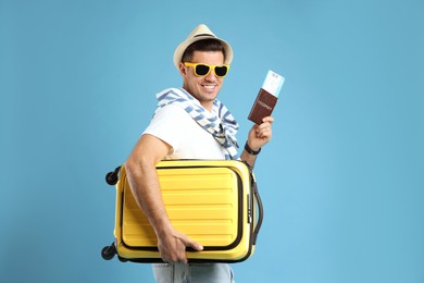 Male tourist holding passport with ticket and suitcase on turquoise background Photo of Male tourist holding passport with ticket and suitcase on turquoise background