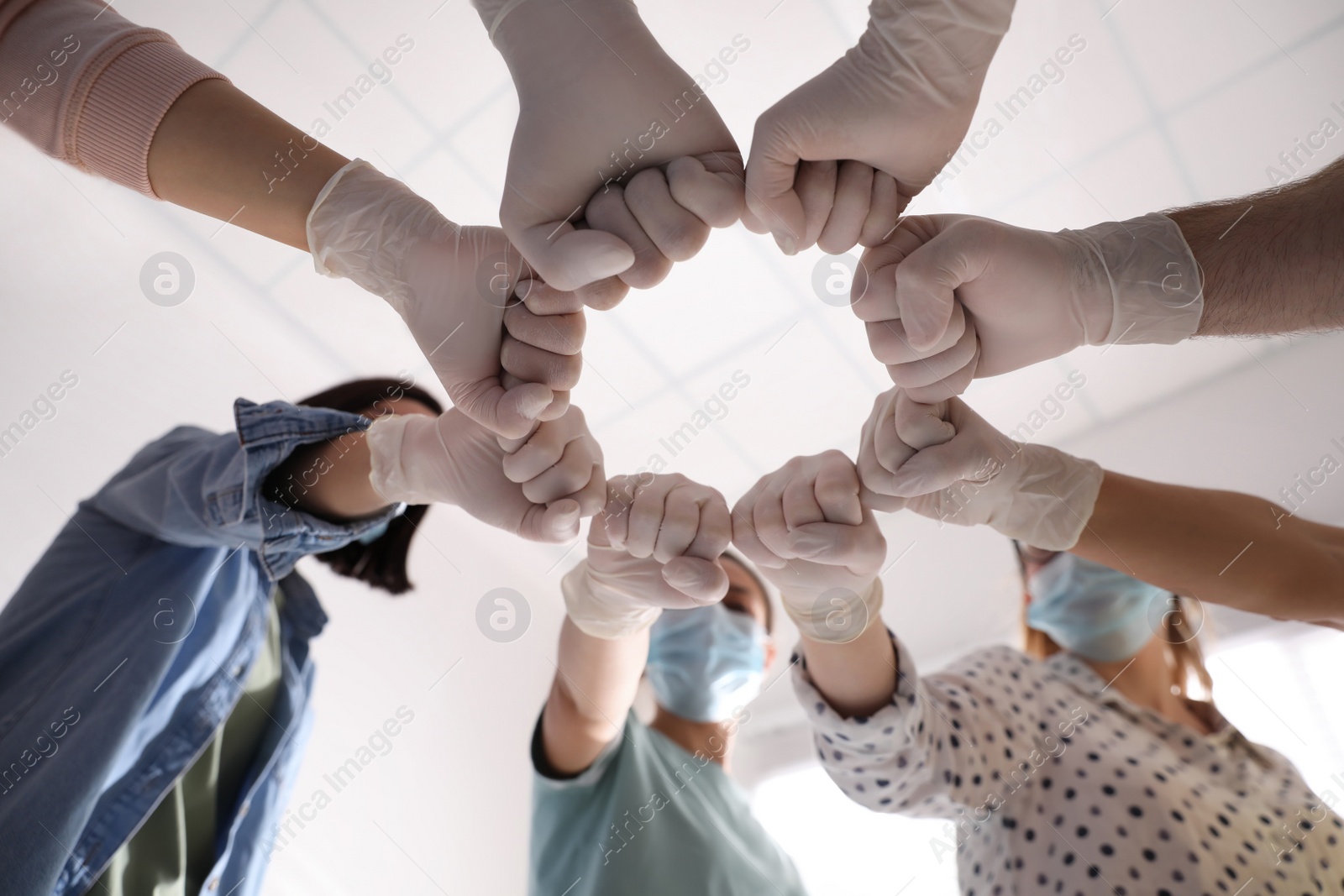 People in white medical gloves joining fists on light background, low angle view Photo of People in white medical gloves joining fists on light background, low angle view