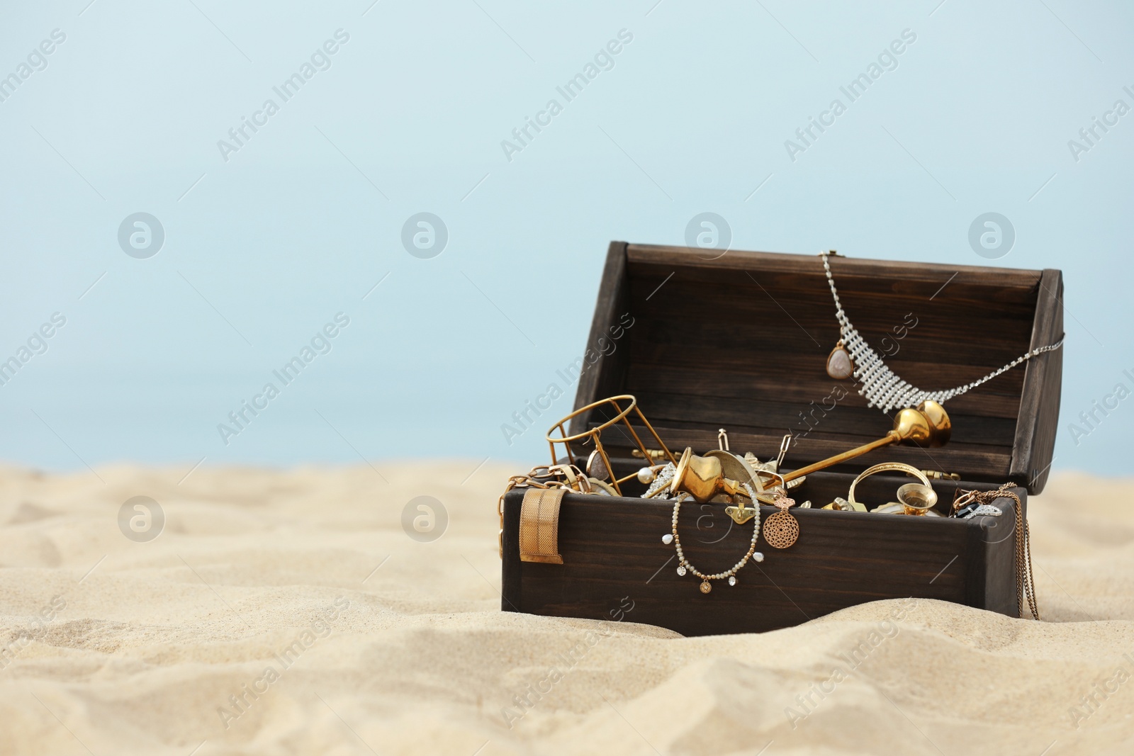 Open wooden chest with treasures on sandy beach, space for text Photo of Open wooden chest with treasures on sandy beach, space for text