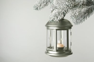 Christmas lantern with candle hanging on snowy fir tree branch against light background. Space for text Photo of Christmas lantern with candle hanging on snowy fir tree branch against light background. Space for text