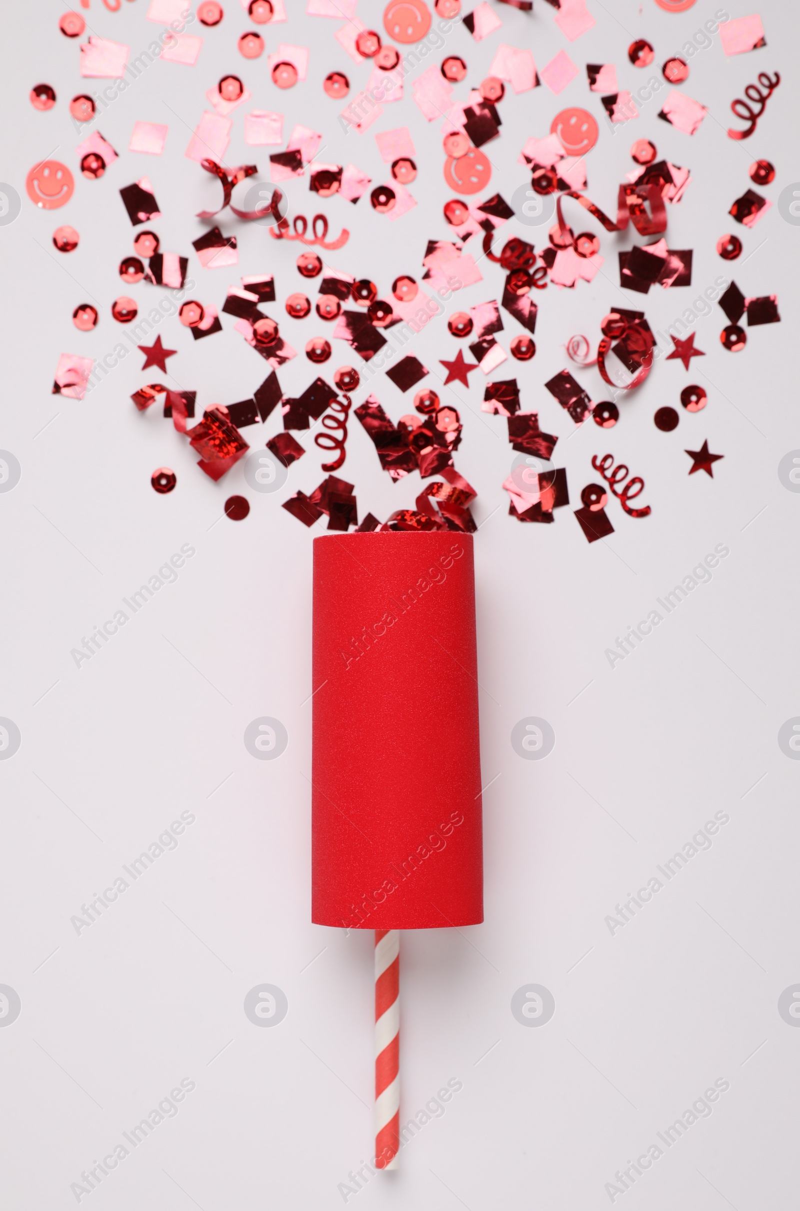 Shiny red confetti bursting out of party cracker on light background, top view Photo of Shiny red confetti bursting out of party cracker on light background, top view