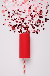 Shiny red confetti bursting out of party cracker on light background, top view Photo of Shiny red confetti bursting out of party cracker on light background, top view