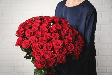 Woman holding luxury bouquet of fresh red roses near white brick wall, closeup Photo of Woman holding luxury bouquet of fresh red roses near white brick wall, closeup