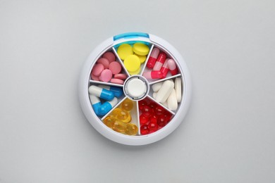 Plastic box with different pills on light grey background, top view Photo of Plastic box with different pills on light grey background, top view