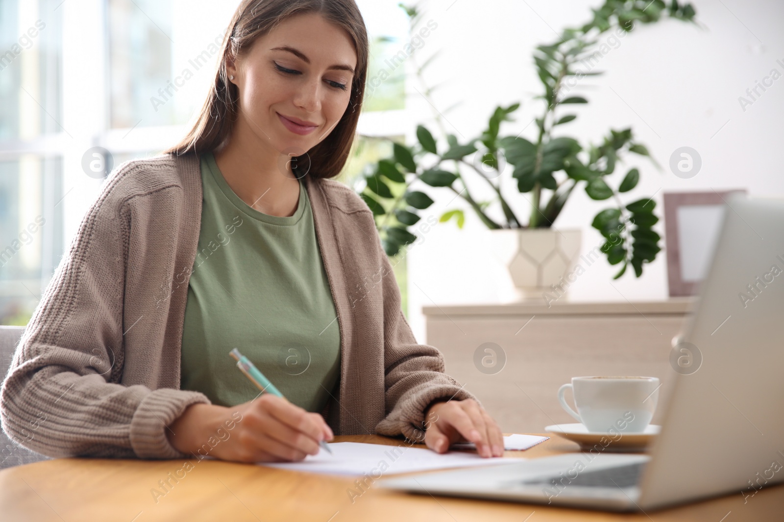 Woman writing letter at wooden table in room Photo of Woman writing letter at wooden table in room