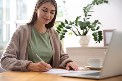 Woman writing letter at wooden table in room Photo of Woman writing letter at wooden table in room