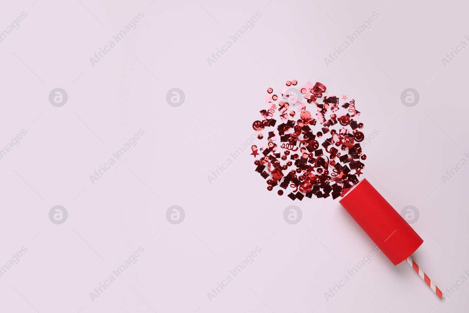 Shiny red confetti bursting out of party cracker on light background, top view. Space for text Photo of Shiny red confetti bursting out of party cracker on light background, top view. Space for text