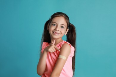 Vaccinated little girl showing medical plaster on her arm against light blue background Photo of Vaccinated little girl showing medical plaster on her arm against light blue background