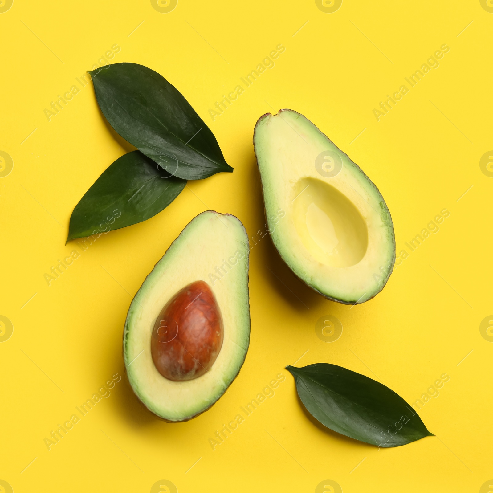 Cut ripe avocado and green leaves on yellow background, flat lay Photo of Cut ripe avocado and green leaves on yellow background, flat lay