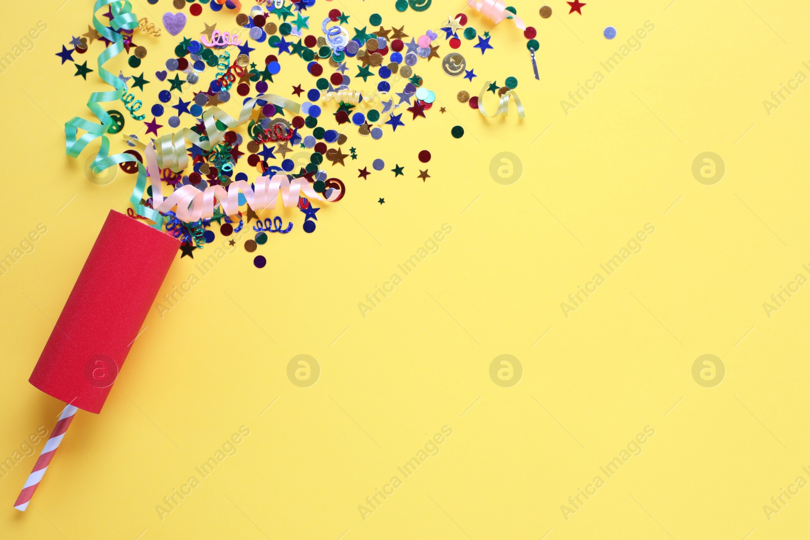 Colorful confetti and streamers with red party cracker on yellow background, top view. Space for text Photo of Colorful confetti and streamers with red party cracker on yellow background, top view. Space for text