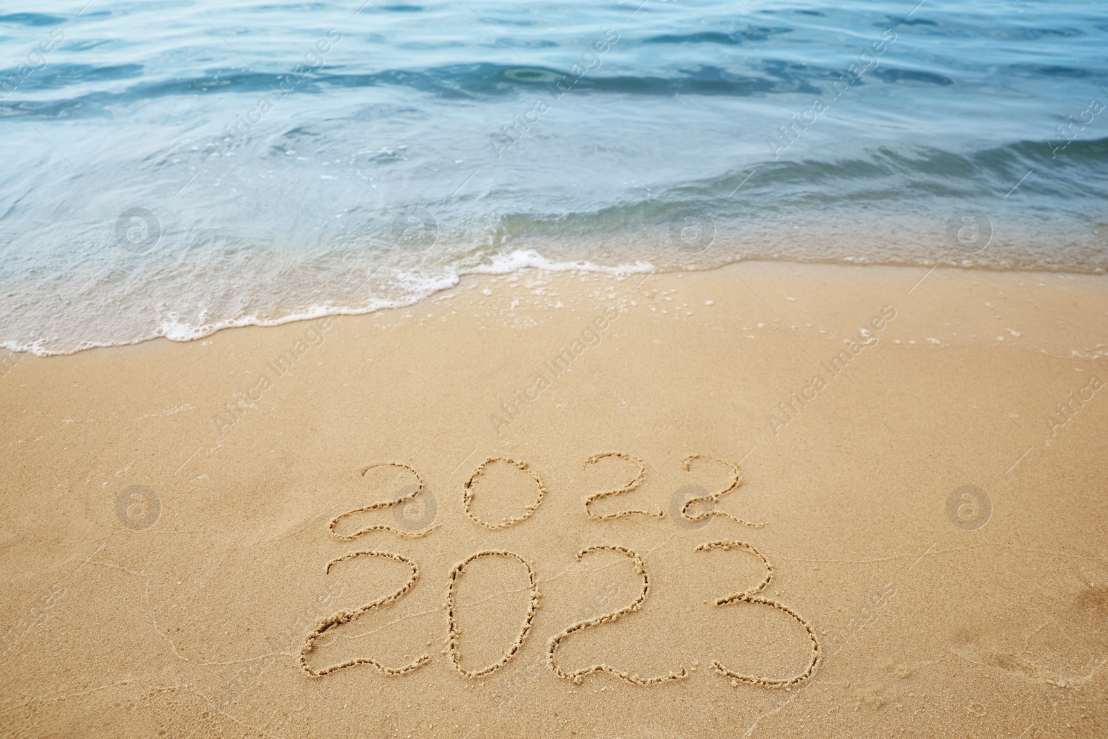 Dates written on sandy beach. 2022 washed by sea wave as New 2023 Year coming Photo of Dates written on sandy beach. 2022 washed by sea wave as New 2023 Year coming