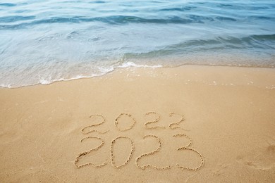 Dates written on sandy beach. 2022 washed by sea wave as New 2023 Year coming Photo of Dates written on sandy beach. 2022 washed by sea wave as New 2023 Year coming