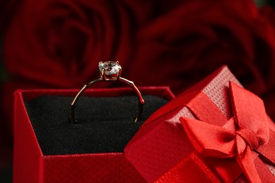 Beautiful engagement ring with gemstone in box against roses, closeup Photo of Beautiful engagement ring with gemstone in box against roses, closeup