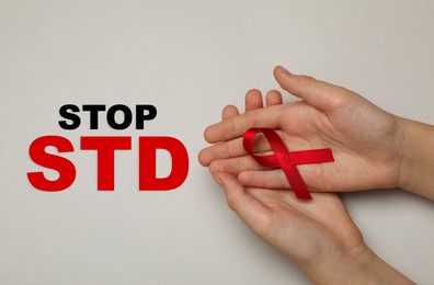 Young woman holding red awareness ribbon on beige background, top view. Stop STD Image of Young woman holding red awareness ribbon on beige background, top view. Stop STD