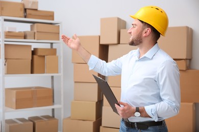 Young man with clipboard near cardboard boxes at warehouse Photo of Young man with clipboard near cardboard boxes at warehouse