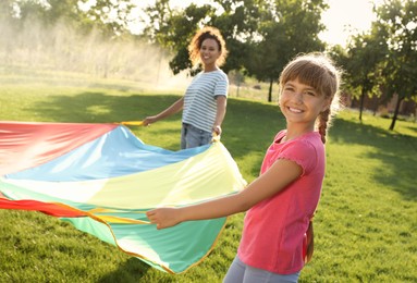 Cute child and African-American teacher playing with rainbow playground parachute on green grass. Summer camp activity Photo of Cute child and African-American teacher playing with rainbow playground parachute on green grass. Summer camp activity