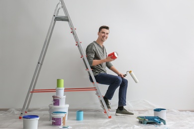 Male decorator sitting on ladder in empty room Photo of Male decorator sitting on ladder in empty room