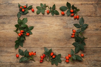 Frame of ripe rose hip berries with green leaves on wooden table, flat lay. Space for text Photo of Frame of ripe rose hip berries with green leaves on wooden table, flat lay. Space for text