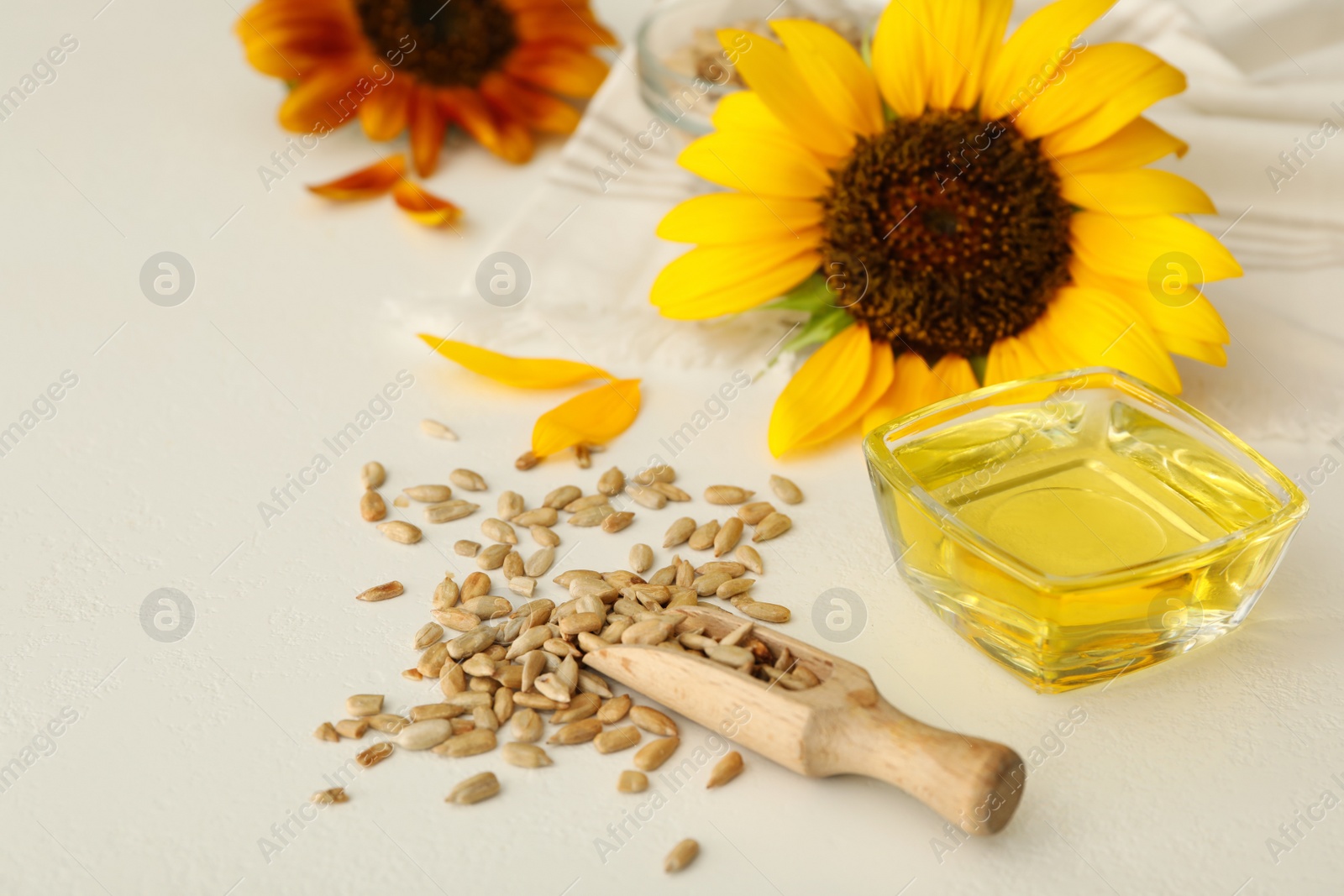 Sunflower oil in glass bowl and seeds on white table Photo of Sunflower oil in glass bowl and seeds on white table