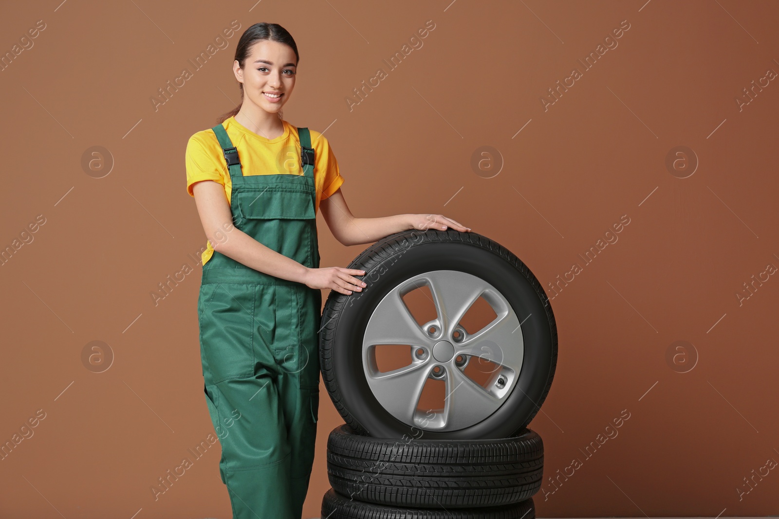 Female mechanic in uniform with car tires on color background Photo of Female mechanic in uniform with car tires on color background