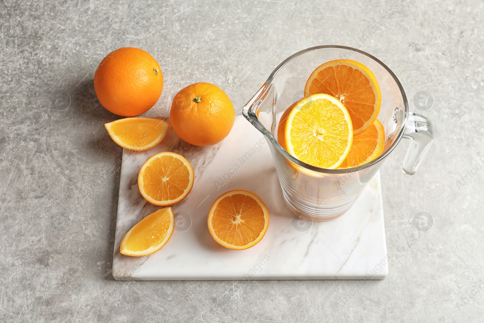 Jug with fresh oranges on marble board. Making juice Photo of Jug with fresh oranges on marble board. Making juice