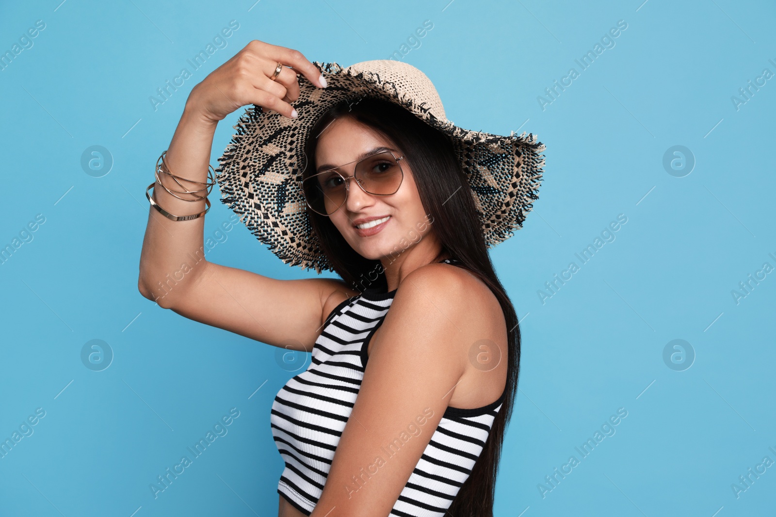 Beautiful young woman with straw hat and stylish sunglasses on light blue background Photo of Beautiful young woman with straw hat and stylish sunglasses on light blue background