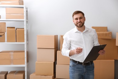 Young businessman with clipboard near cardboard boxes at warehouse Photo of Young businessman with clipboard near cardboard boxes at warehouse
